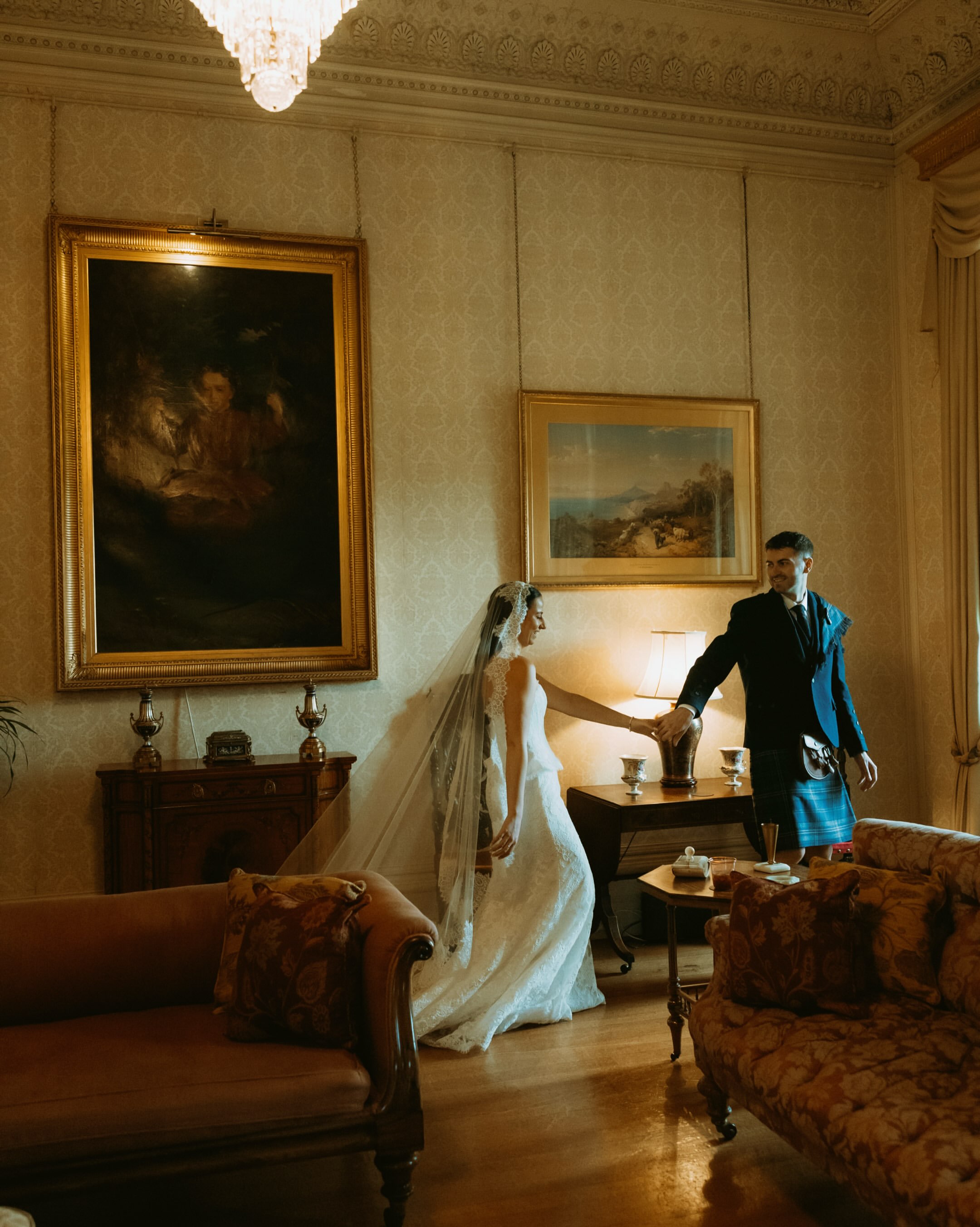 Bride and groom reaching for each other in a lamplit parlor