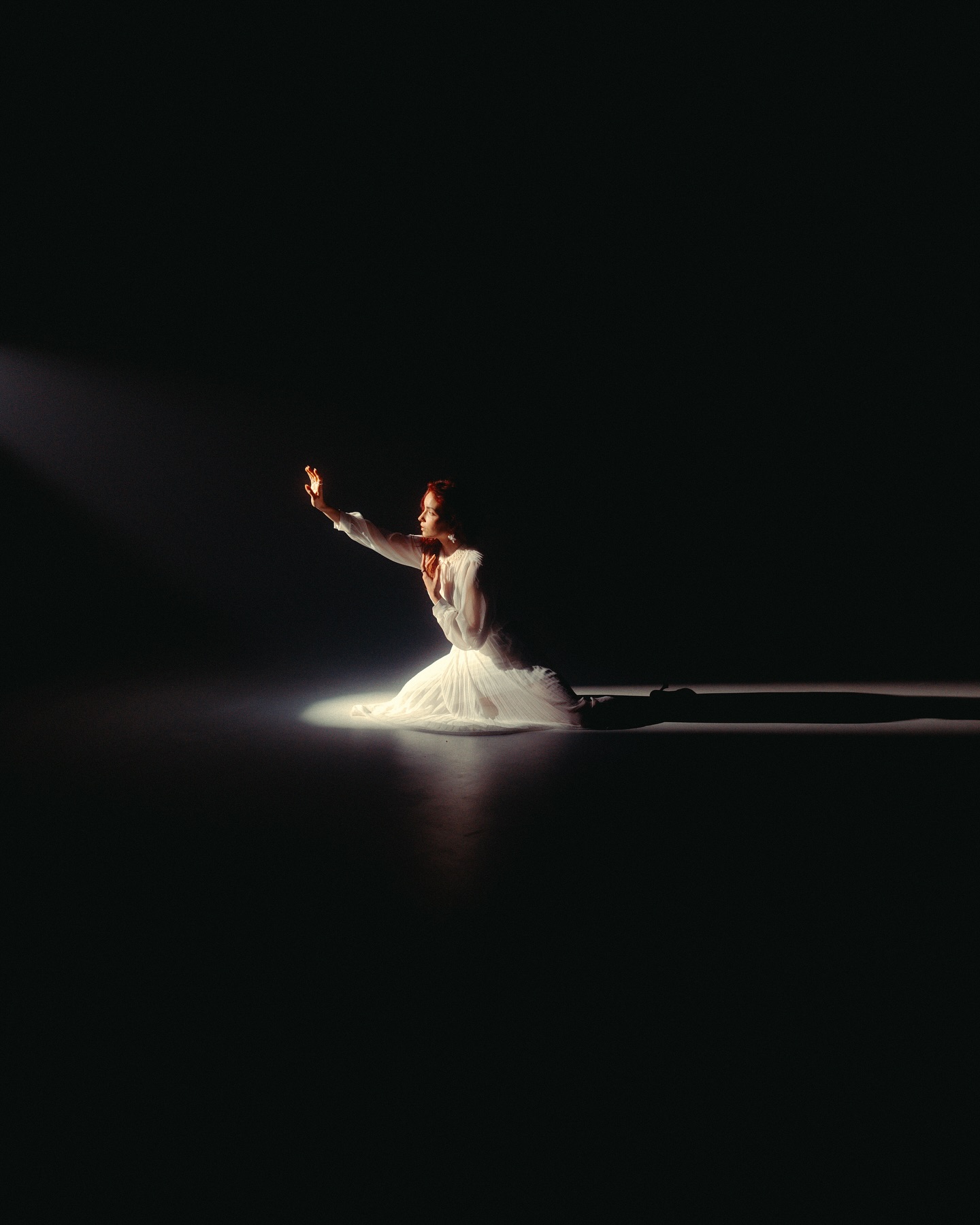 Figure in a white dress reaching into a single beam of light